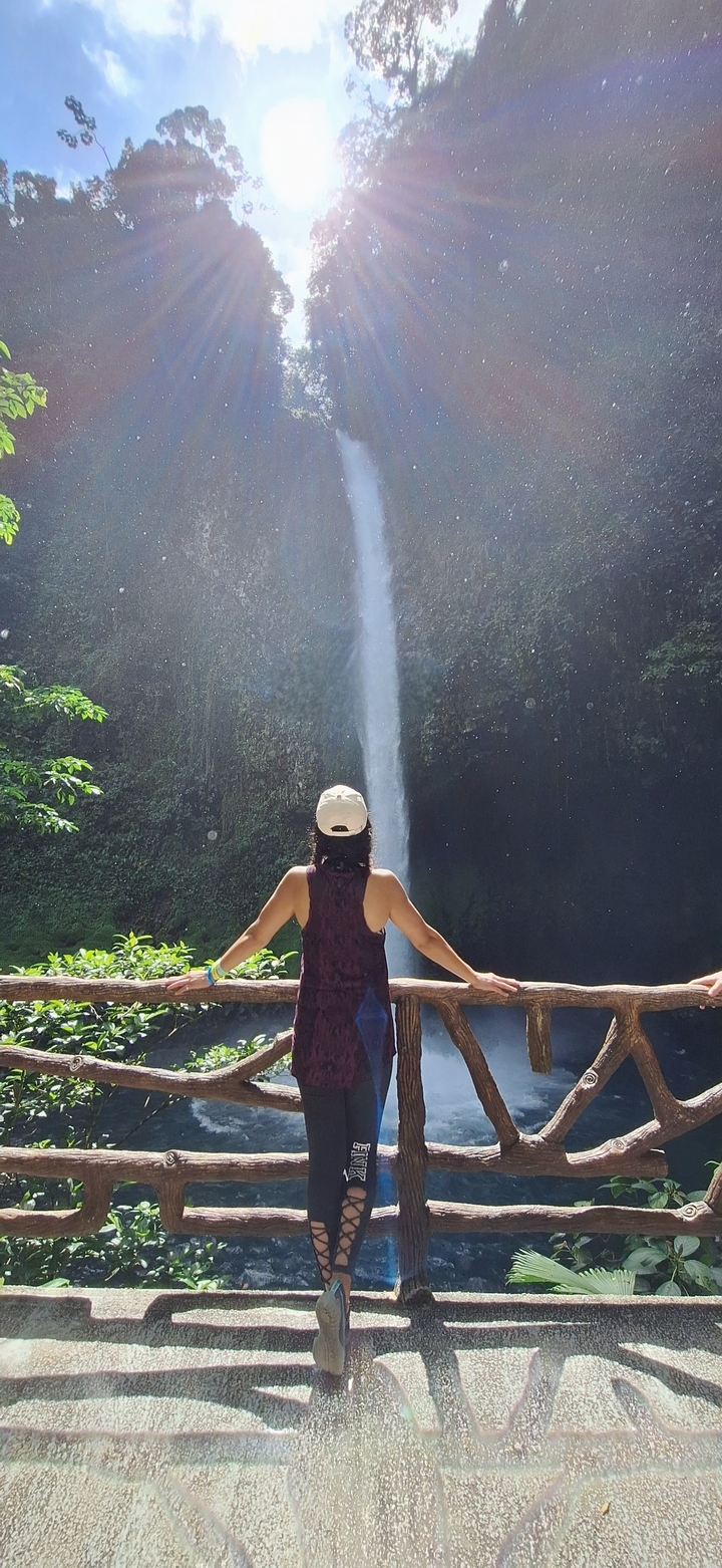 Person standing with arms wide open in front of a waterfall.