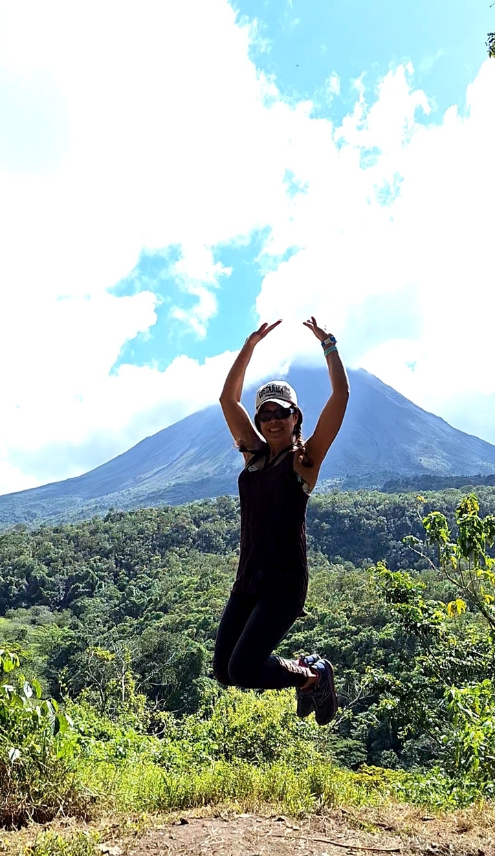 Person posing with the backdrop of a volcano.