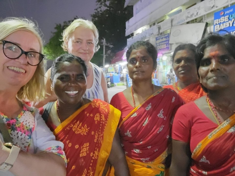Groupe de femmes en tenues traditionnelles colorées posant avec un touriste.