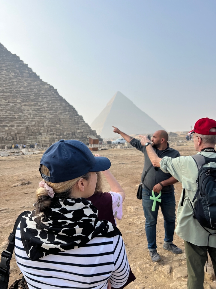 Des touristes pointent du doigt les grandes pyramides en arrière-plan.