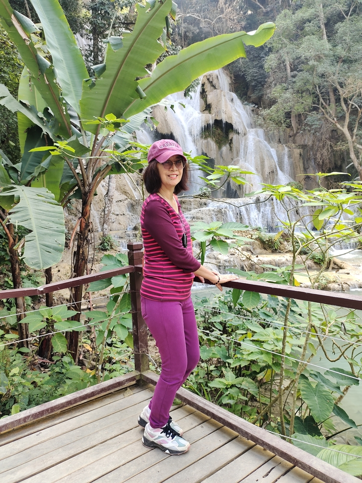 Femme en tenue rose debout sur un pont près d'une cascade.