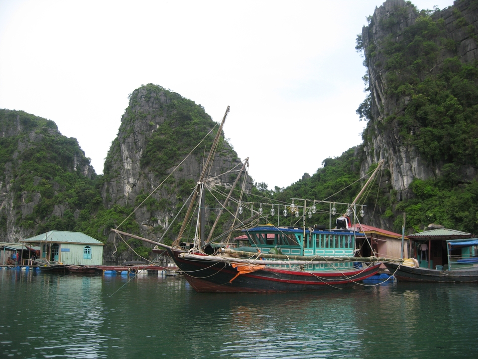 Traditional boat docked near floating structures with steep cliffs.