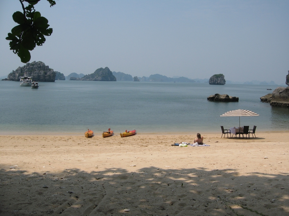 Person relaxing on a beach with kayaks and islands in the distance.