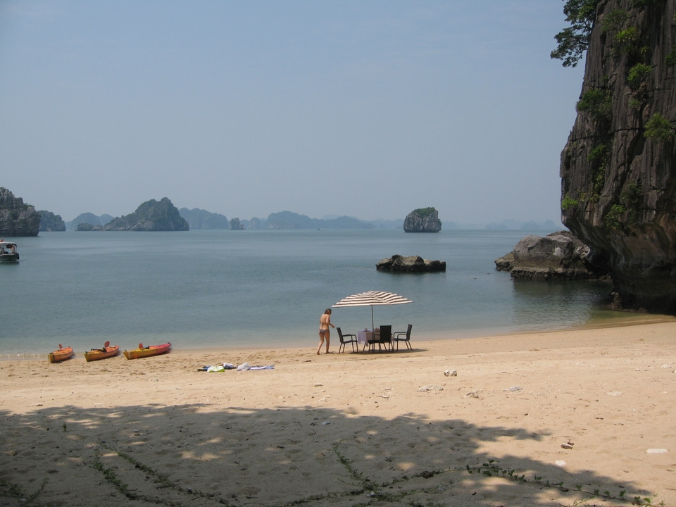 Personne marchant sur une plage avec des kayaks et des îles en arrière-plan.