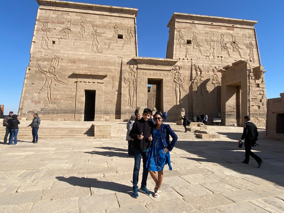 Deux personnes devant un temple égyptien antique avec des murs en pierre sculptée.