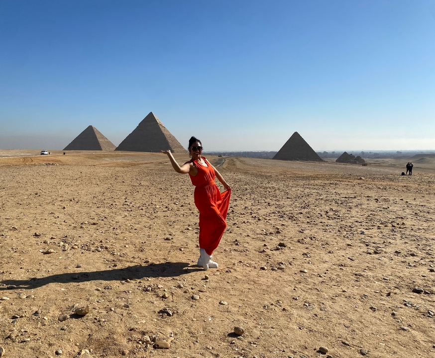 Personne en robe rouge posant avec les pyramides de Gizeh en arrière-plan.