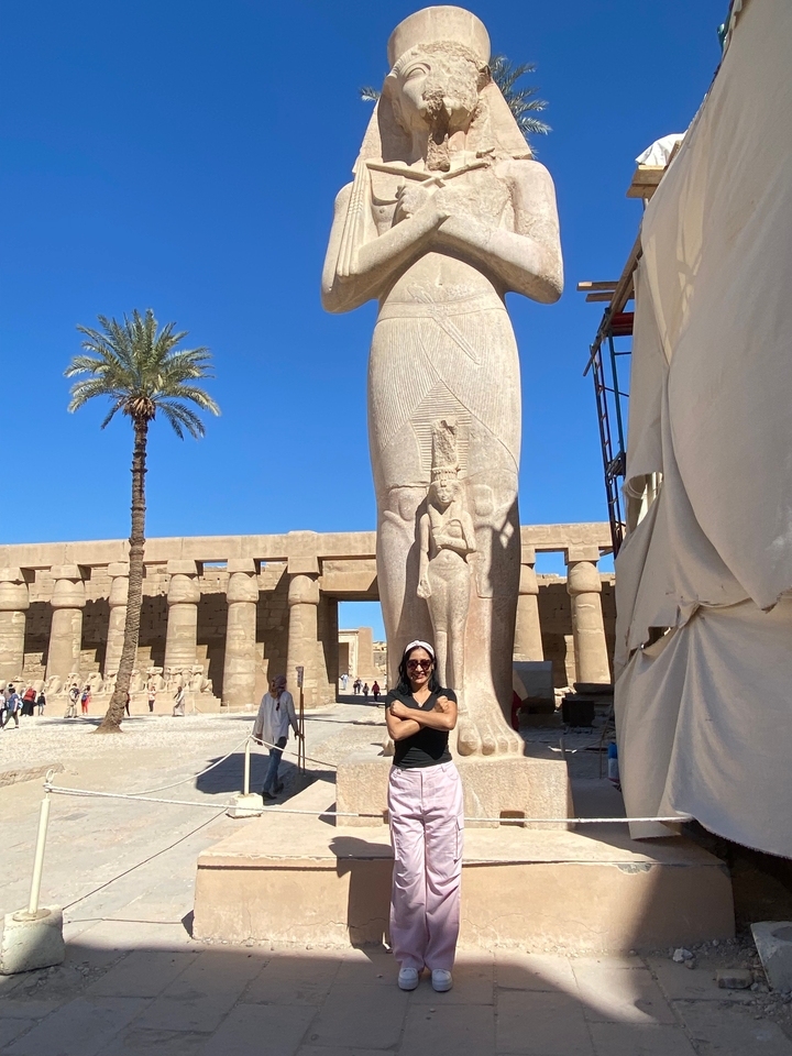 Personne debout devant une statue égyptienne antique et des colonnes de temple.