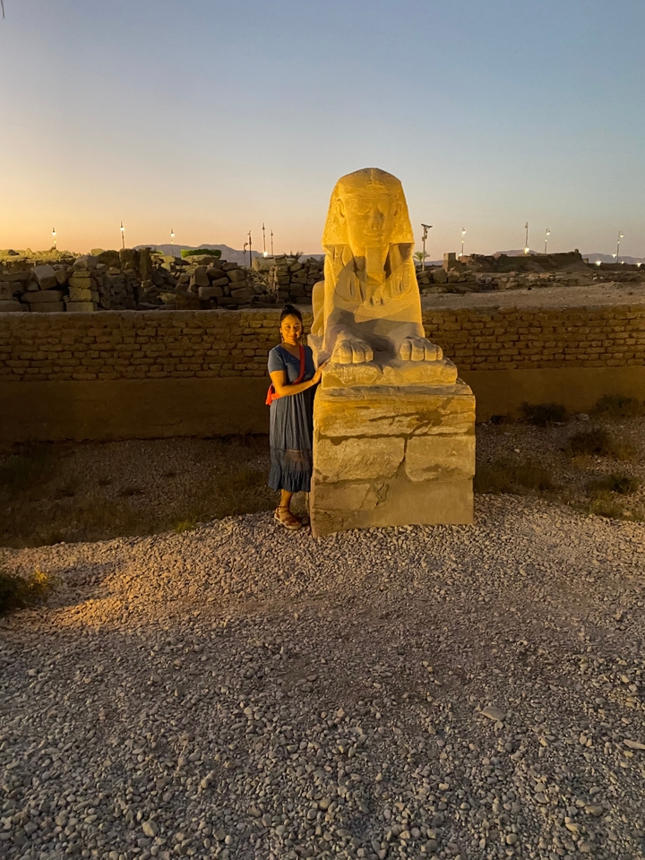 Personne debout à côté de la patte d'une statue dans un site archéologique la nuit.
