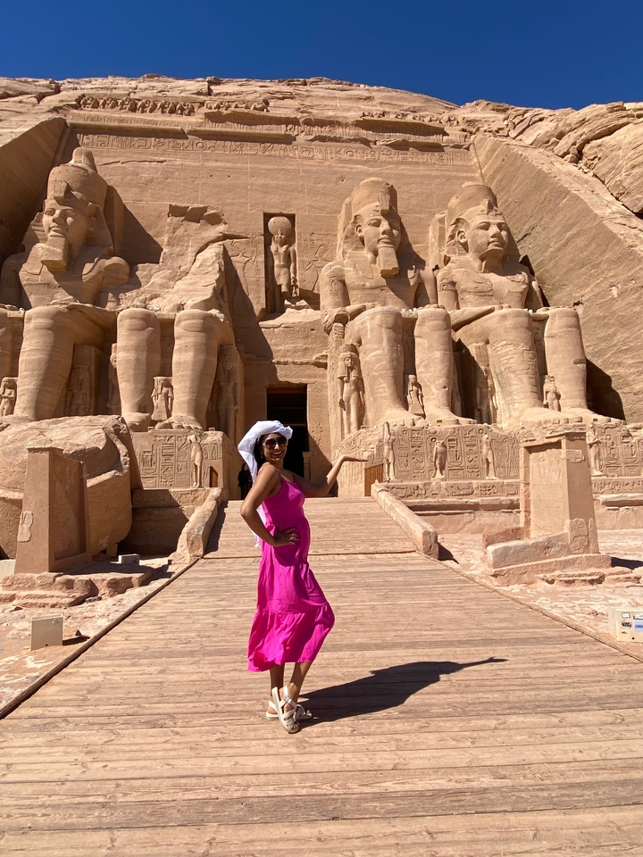 Personne en robe rose debout devant les temples d'Abou Simbel.