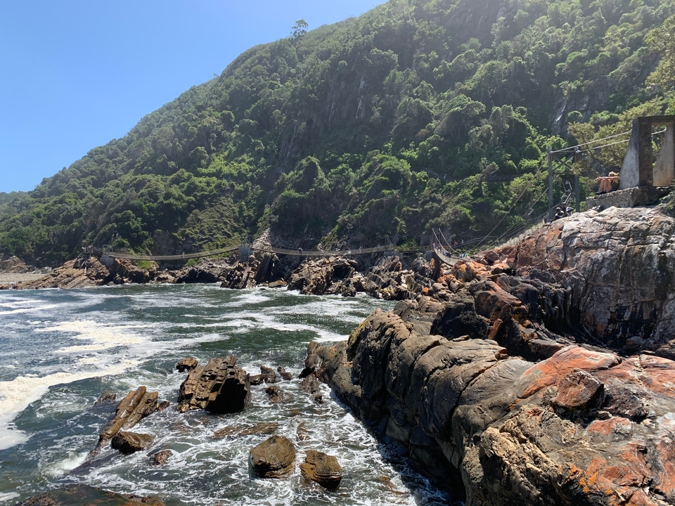 Suspension bridge over rocky coast with ocean waves.