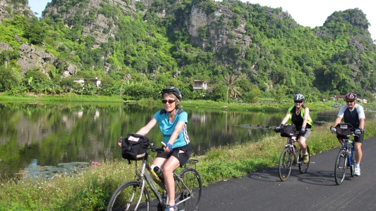 Cyclists riding along a scenic path with mountains and lake in the background.
