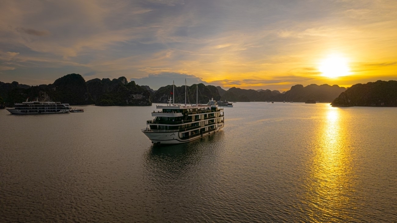 Bateau de croisière sur l'eau au coucher du soleil entouré de montagnes karstiques.