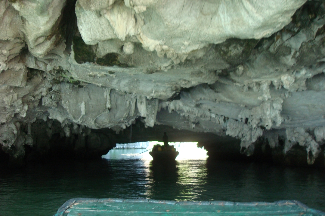 Shadowy outline of a boat inside a vast limestone grotto with daylight glowing at the exit