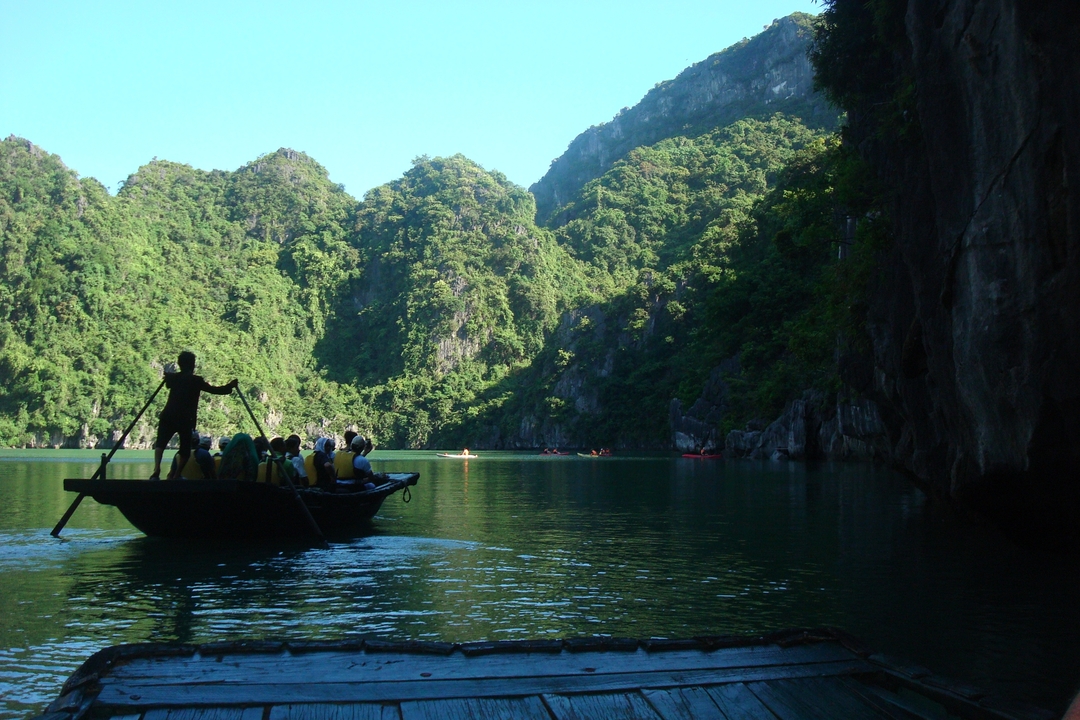 Paddle boat with tourists on a jade-green lagoon surrounded by towering jungle-covered cliffs