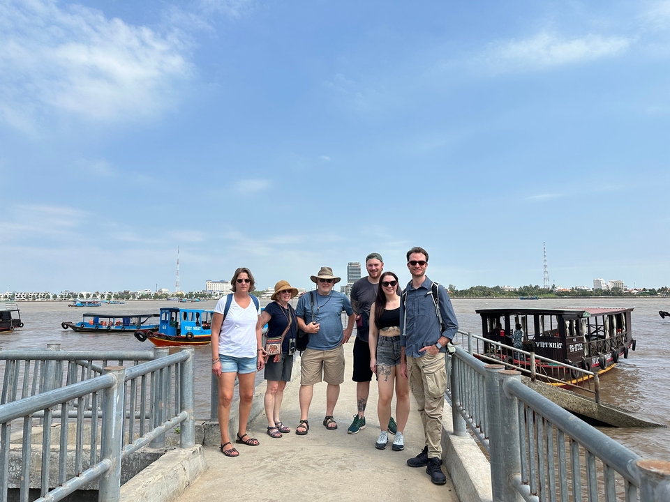 Groupe de personnes debout sur un quai avec des bateaux sur la rivière et des bâtiments en arrière-plan.