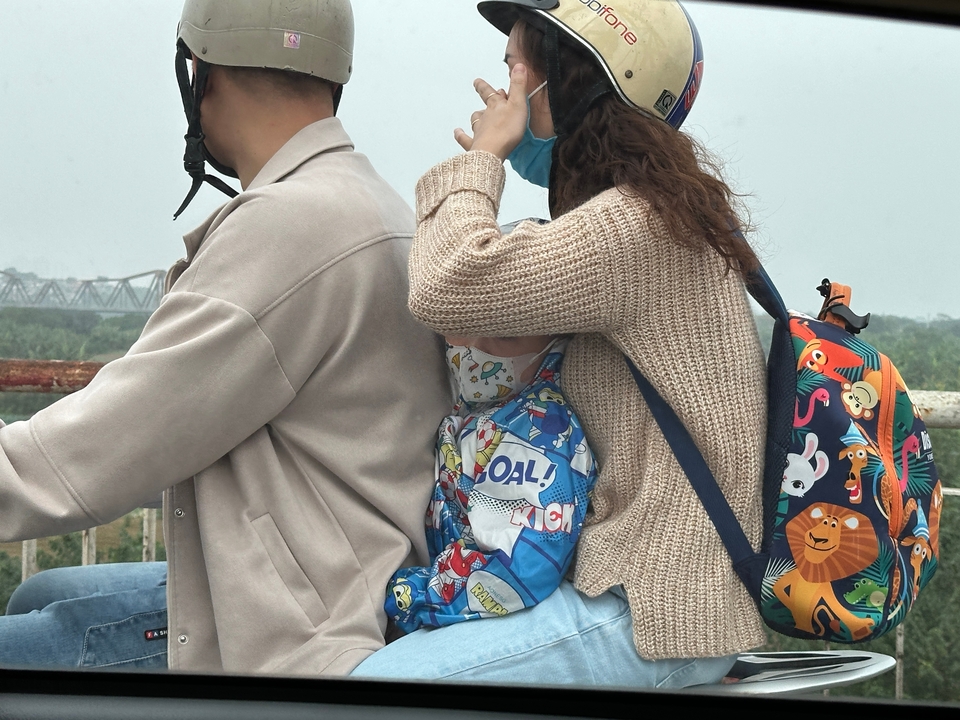 Two adults and a child on a motorbike surrounded by nature.