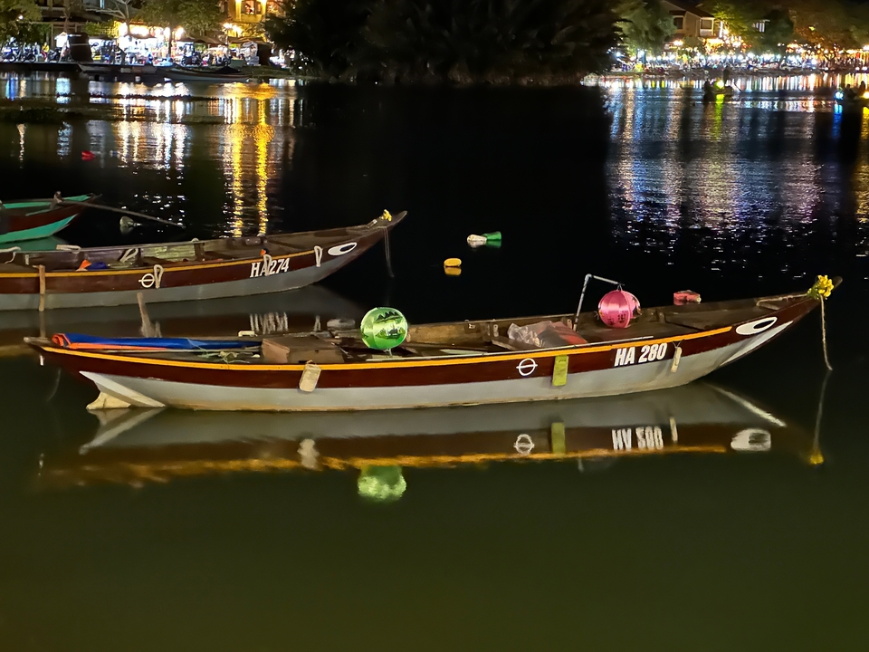 Wooden boats with colorful decorations reflecting in water at night.