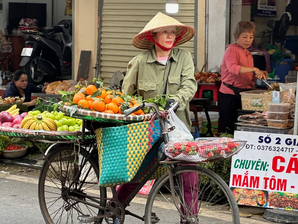 Vendor wearing a conical hat selling fruits on a bicycle in a market.