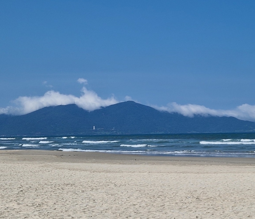 Sandy beach with waves and mountain in the background.