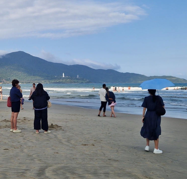 People walking and standing on beach with mountains.