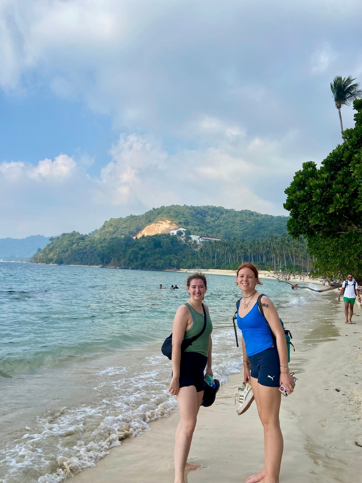 Deux personnes debout sur une plage avec des collines en arrière-plan.
