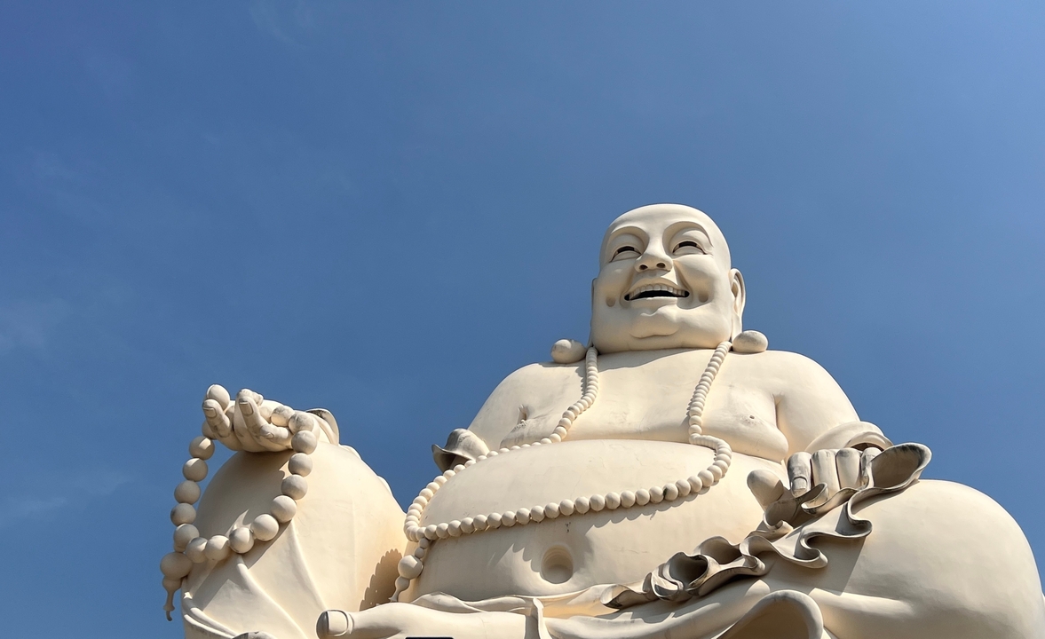 Une grande statue blanche d'un Bouddha avec un ciel bleu clair en arrière-plan.