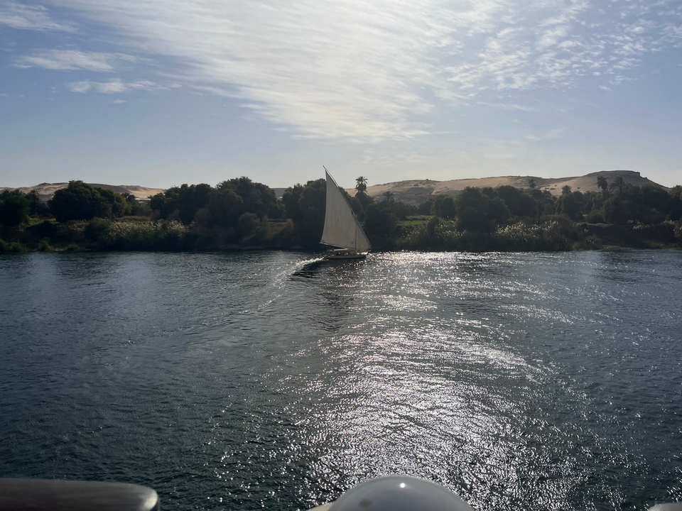 A sailboat on a river with a backdrop of sand dunes.