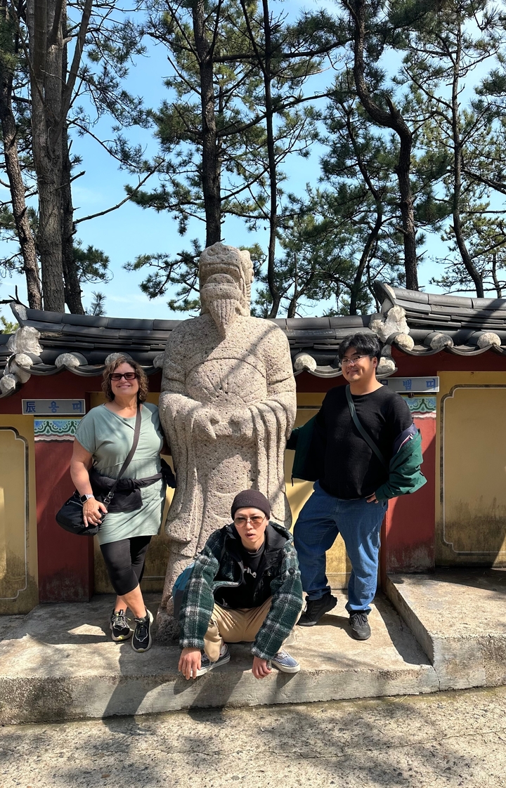 Trois personnes posant à côté d'une statue de pierre dans un parc.