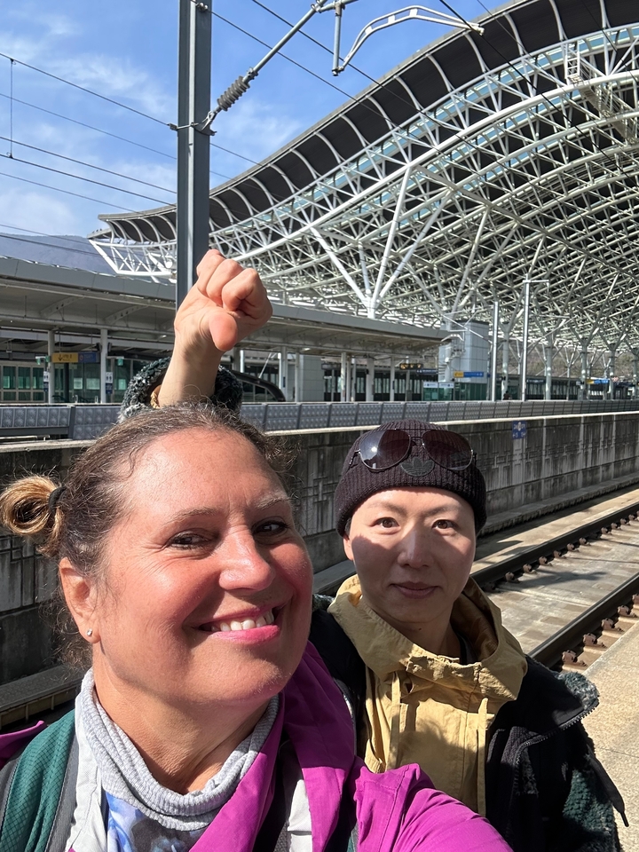 Deux personnes posant dans une gare avec un grand toit métallique.