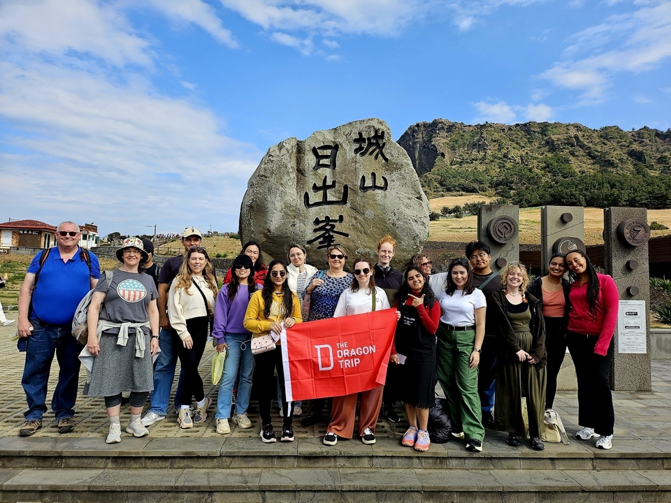 Groupe de personnes posant devant un rocher avec de l'écriture coréenne.