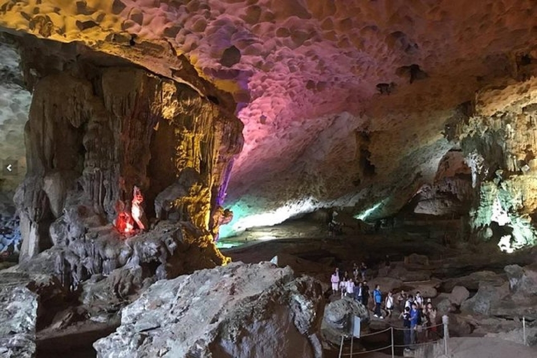 Grande grotte avec éclairage coloré et visiteurs.
