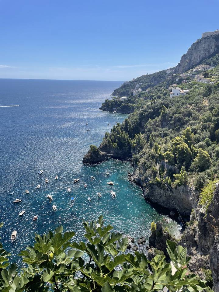 A scenic view of a coastline with cliffs and boats in the clear blue sea.