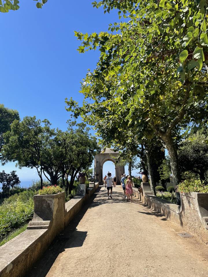 People walking under a stone archway in a park.
