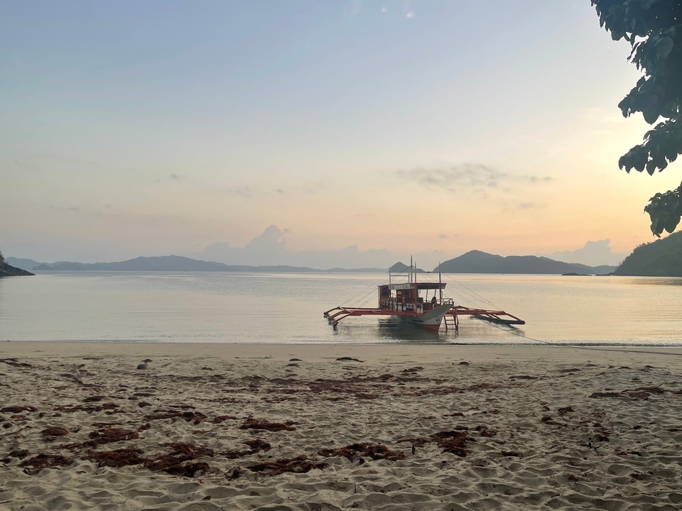 Un bateau traditionnel ancré sur une plage calme au coucher du soleil.