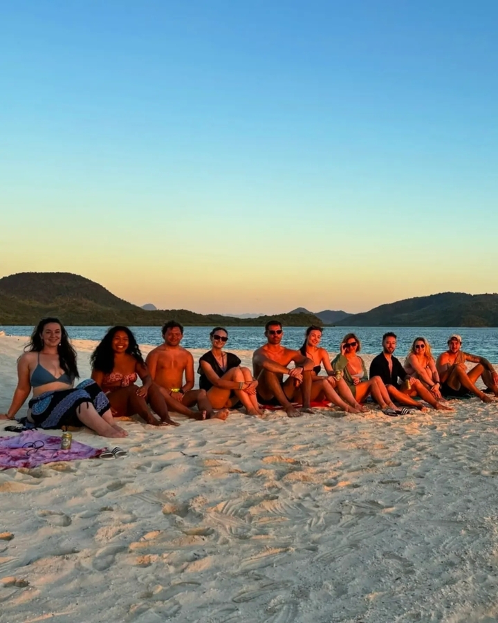 Groupe de personnes assises sur une plage au coucher du soleil.