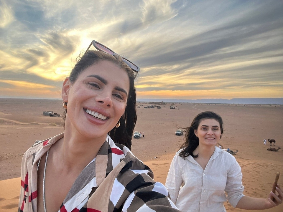 Deux femmes souriantes dans un paysage désertique au coucher du soleil.