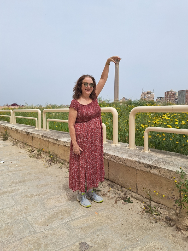 Personne posant dans un cadre extérieur avec des fleurs et un paysage urbain en arrière-plan.