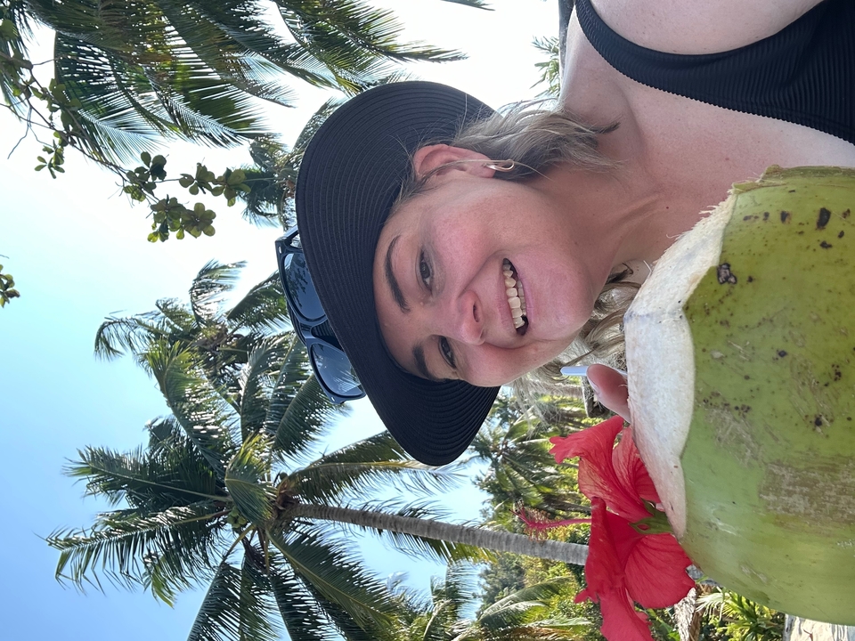 Personne avec une boisson à la noix de coco et des palmiers en arrière-plan.