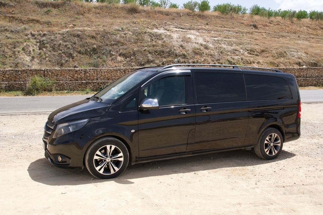 Fourgonnette noire garée sur un chemin de terre avec une clôture en pierre.