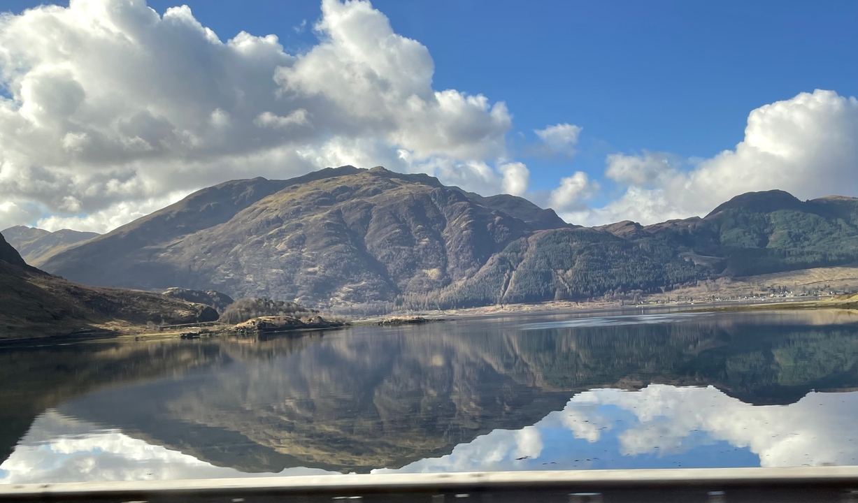 Reflection of mountains in a calm lake under a blue sky with clouds.