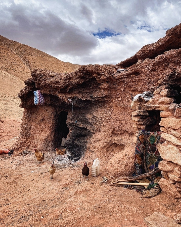 Rough rocky dwelling with items and chickens outside.