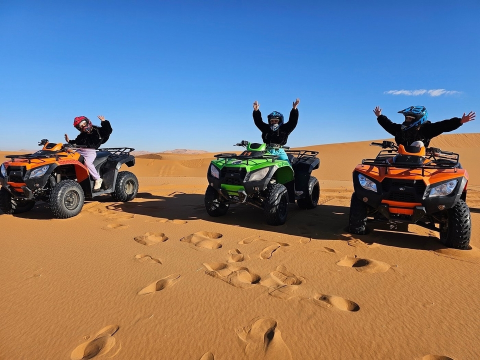 Three people on quad bikes in a desert, raising their hands.
