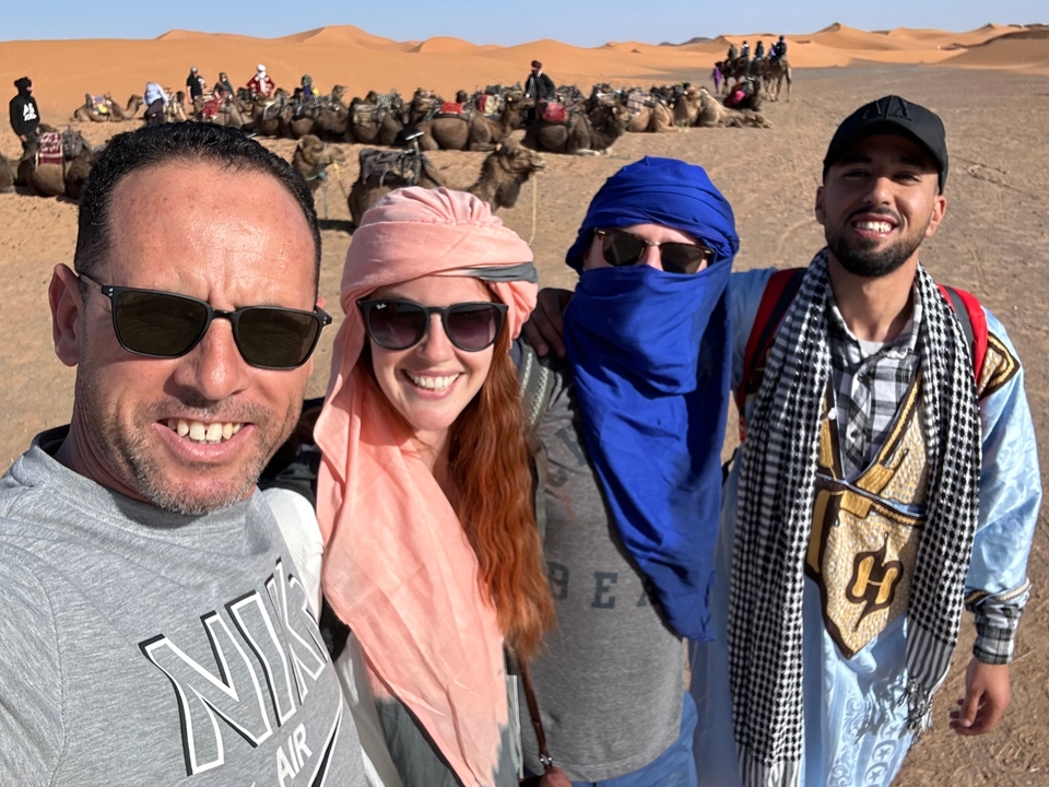 Quatre personnes avec des chameaux portant des foulards traditionnels dans le désert.