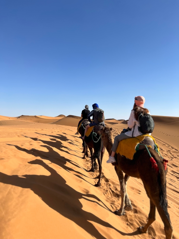Des gens montant des chameaux sur des dunes de sable dans le désert.