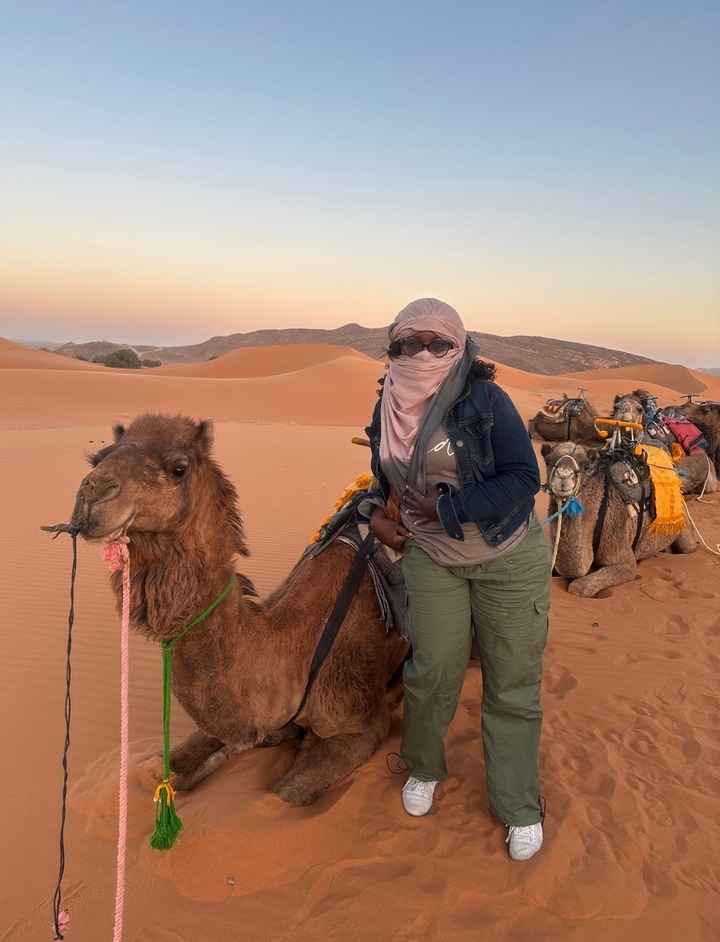 Person posing with a camel in the desert.