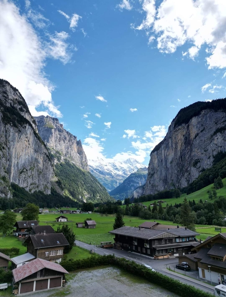 View of a majestic valley with high cliffs, a green landscape, and snow-capped mountains.