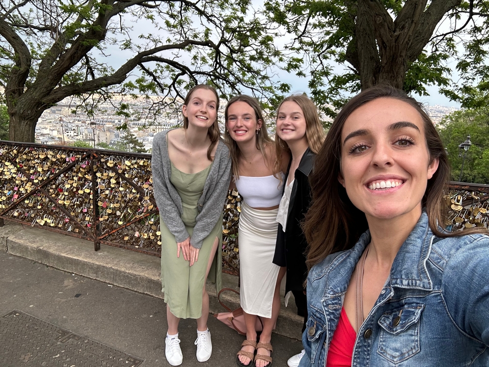 Group of friends posing in front of a love lock bridge with a city in the background.