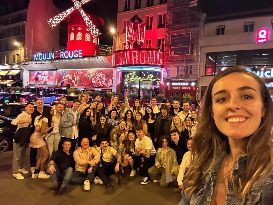 Group of people posing in front of the Moulin Rouge at night.