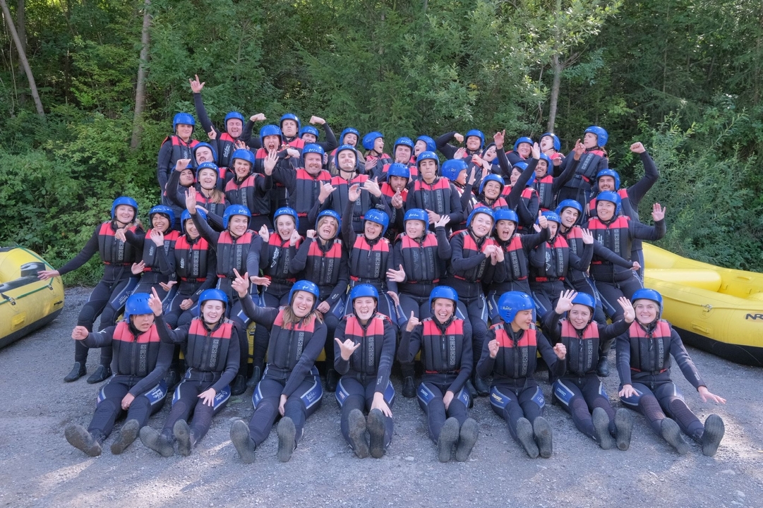 A group of people in wet suits and helmets cheerfully posing, possibly after a rafting activity.