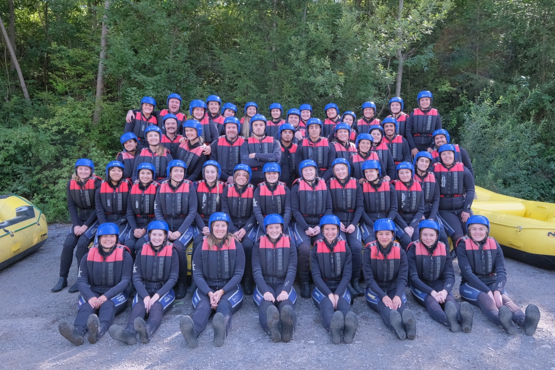 Large group of people in wetsuits and helmets posing for a group photo outdoors.